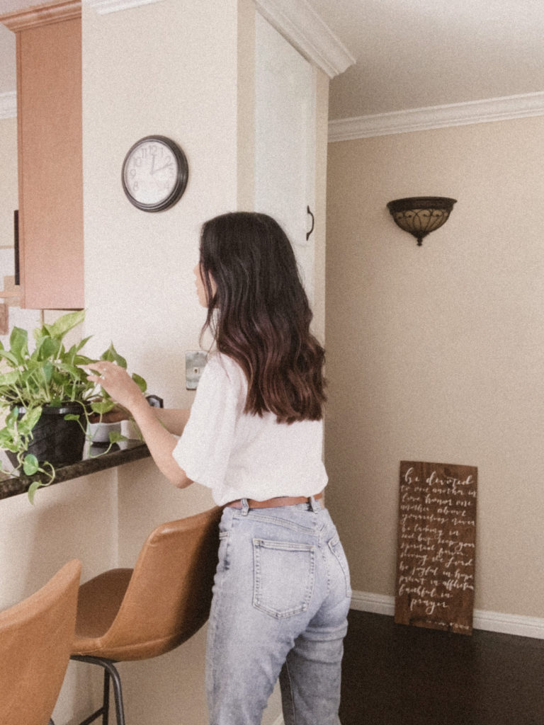Girl standing at kitchen counter reaching out and touching marble queen pothos. 