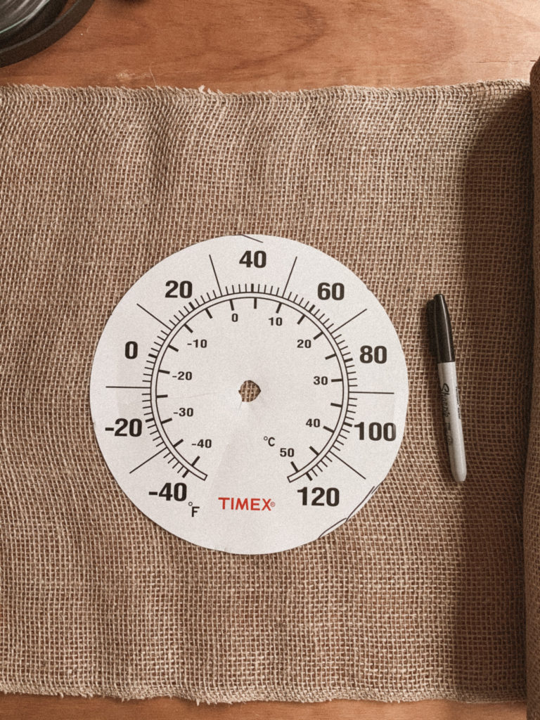 Thermometer face on top of burlap, acting as template for tracing. 