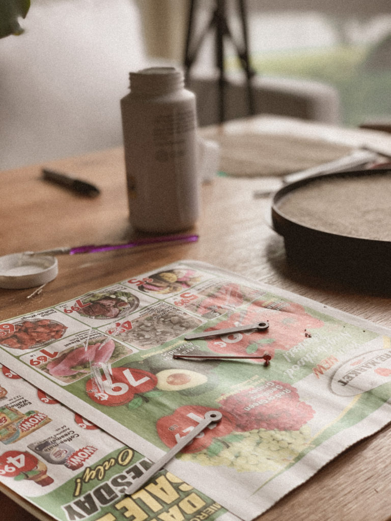 Newly-painted, white clock hands drying on newspaper.