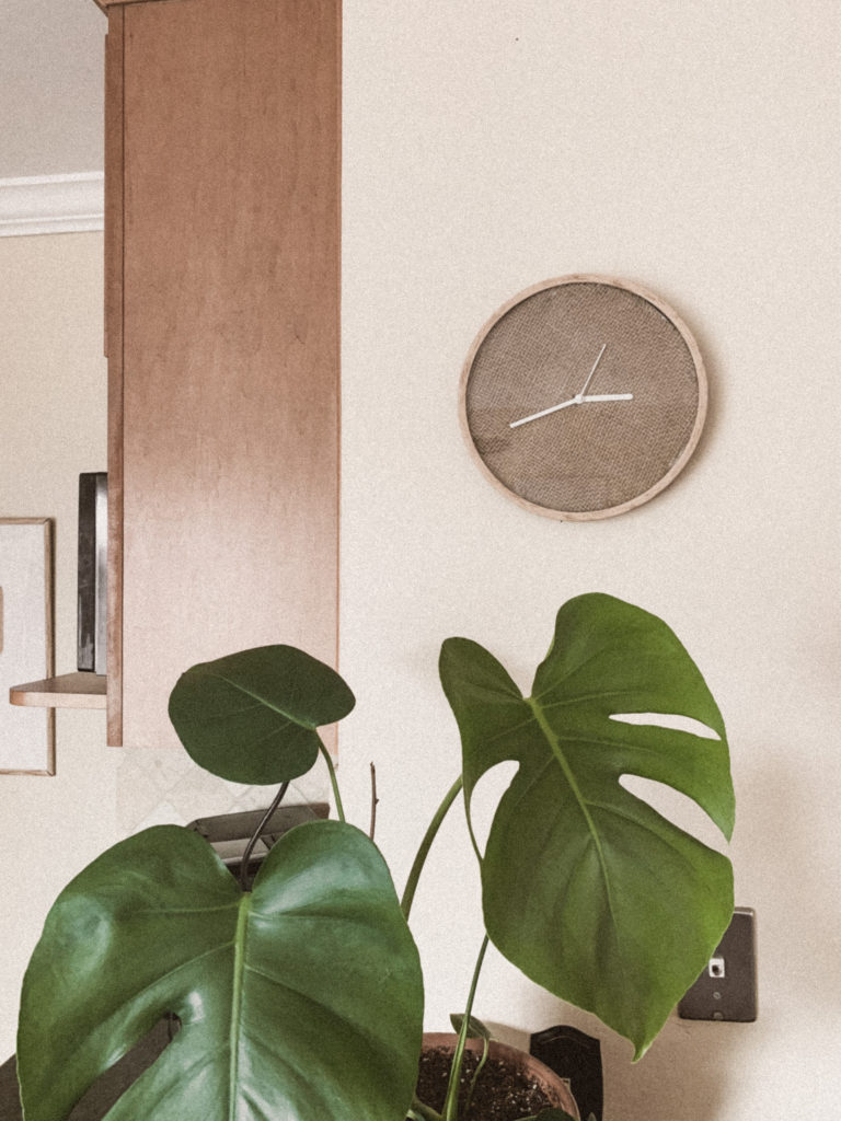 DIY burlap clock on wall, monstera plant in foreground.
