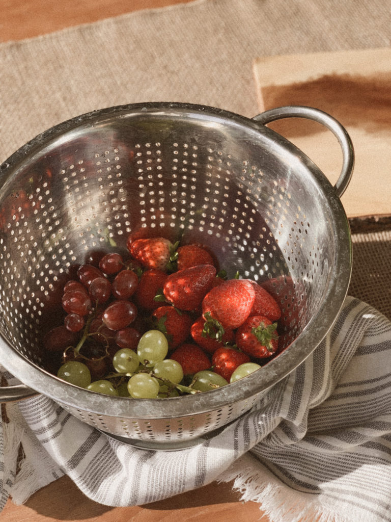Strawberries and grapes in colander, close up photo.