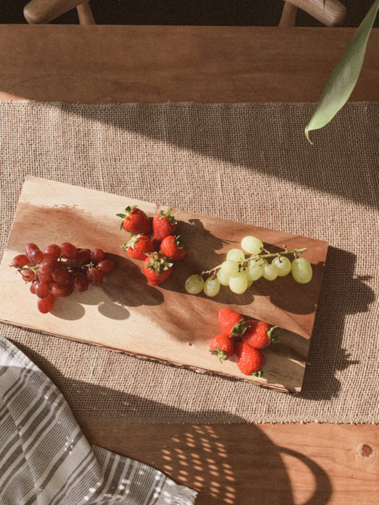 Strawberries and grapes arranged on cheeseboard.