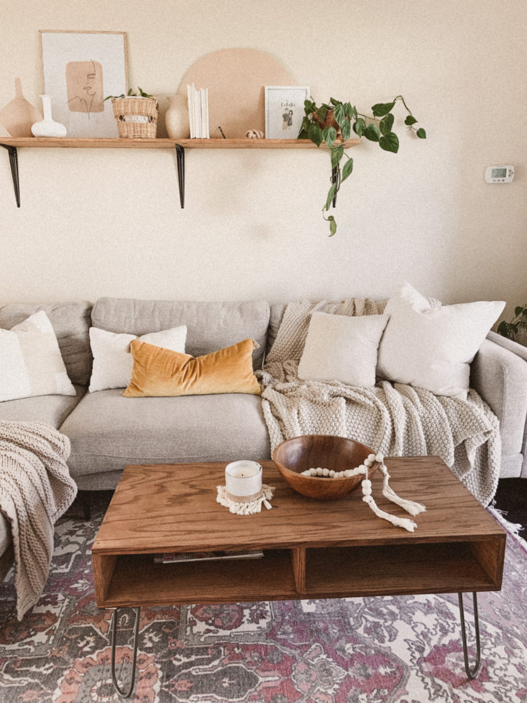 Mid century modern living room with wood shelf above it. Plants, books, and other boho decor accent it.