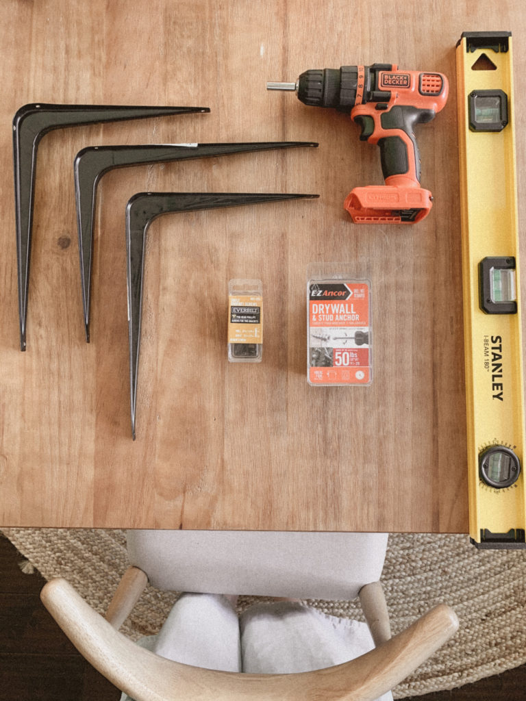 Overhead photo of three black brackets, packets of wall/wood screws, a leveler, and a power drill.