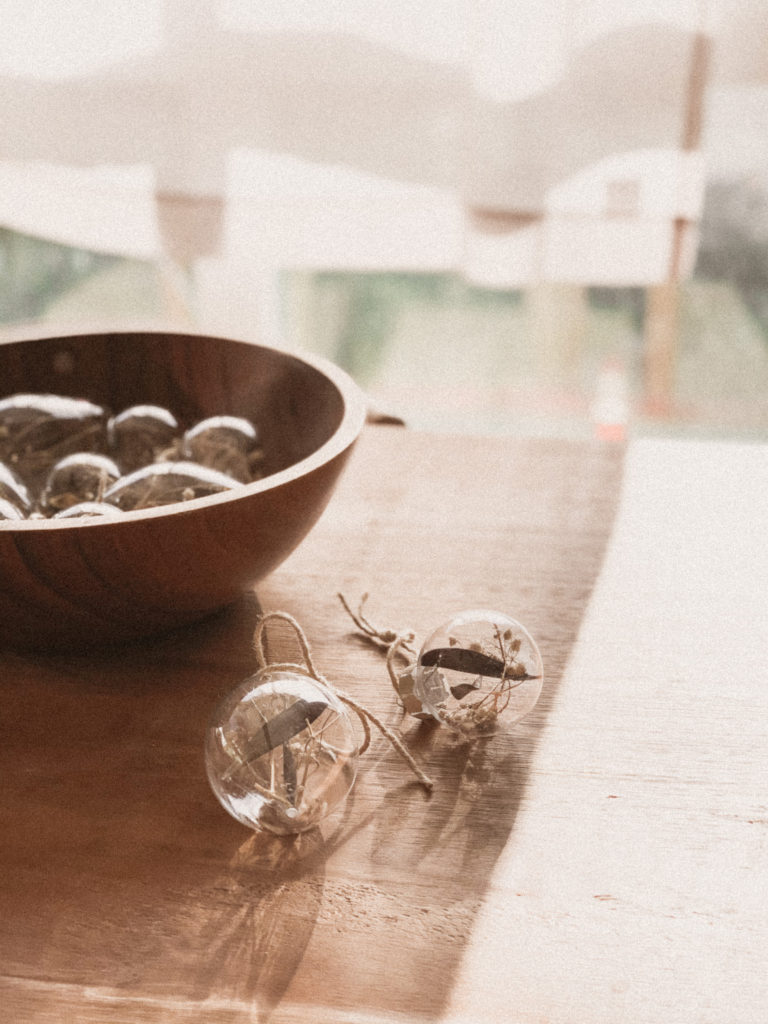 Two filled and finished ornaments on table next to bowl filled with other completed DIY ornaments.