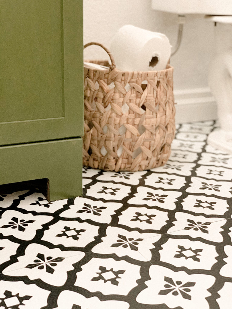 Close up of stick and peel tiles next to wicker basket of toilet paper. 