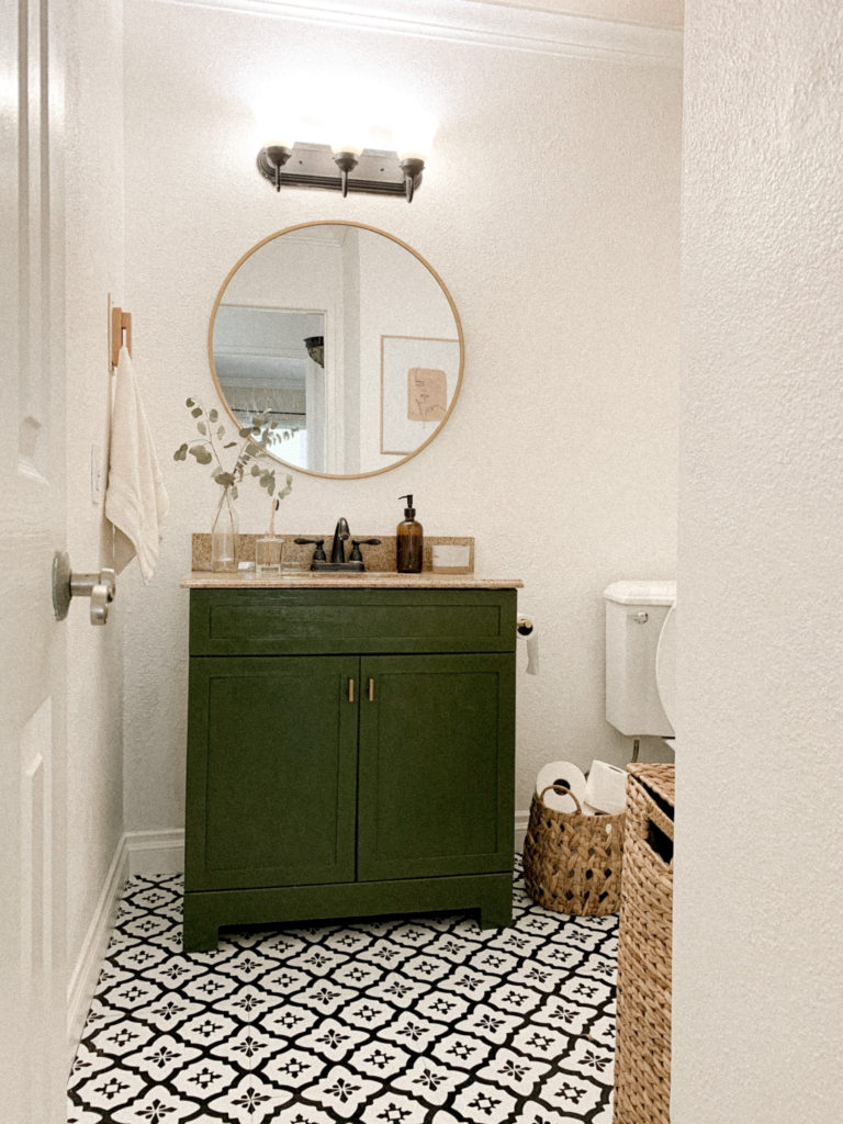 Wide angle of bathroom entrance with white and black, renter friendly stick and peel tiles leading up to green vanity. 