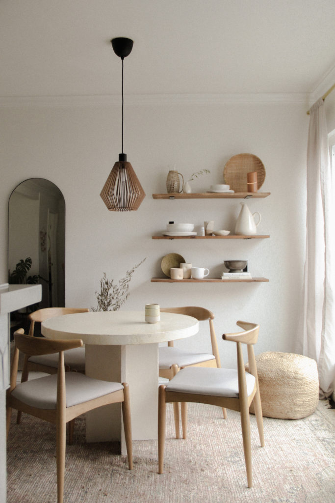 Wide view of neutral dining room with DIY wood shelves on the wall, styled with simple ceramics and decor. 